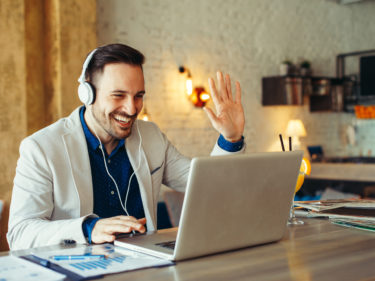 Microsoft Teams Mann mit Headset vor Notebook, der in die Kamera winkt